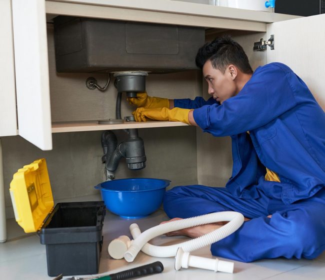 Young Vietnamese plumber checking drain in kitchen